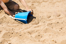 Scooping sand with a bucket.