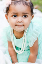 face of an infant girl in a mint green dress with pearls