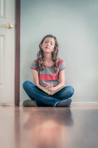 Girl sitting on the floor praying with open bible in her lap