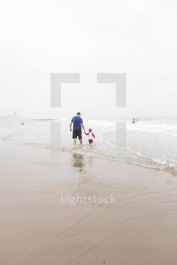 father and son walking in the water on a beach 