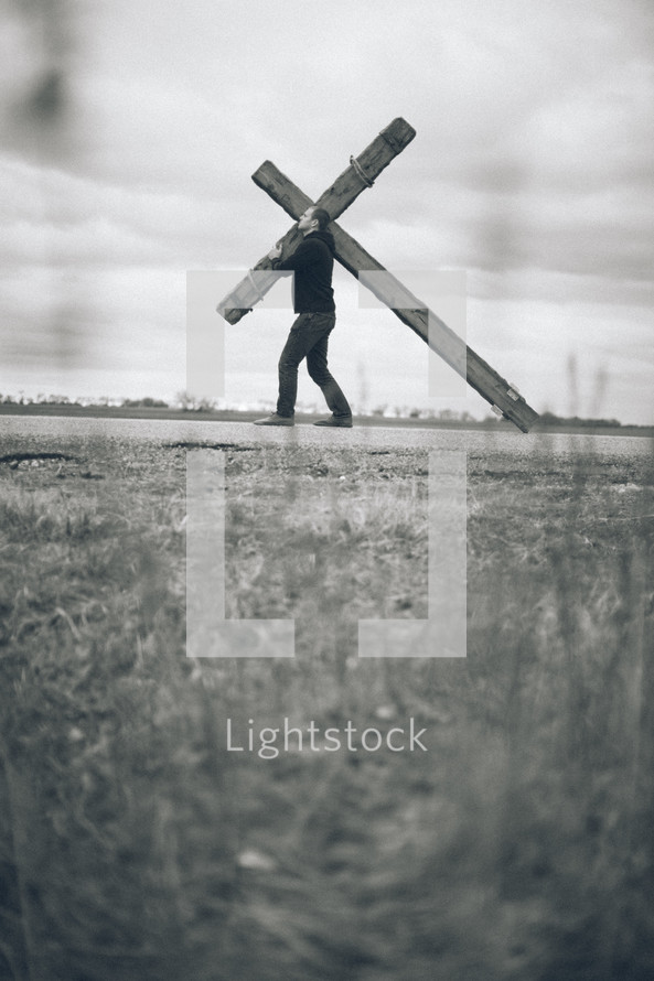 man carrying a large cross along the highway - re-enacting Christ's walk, bearing the cross