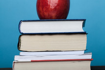 A red apple on top of a stack of books.