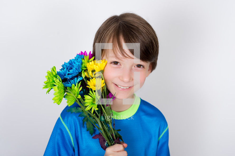 Smiling boy holding a bouquet of flowers by his face.