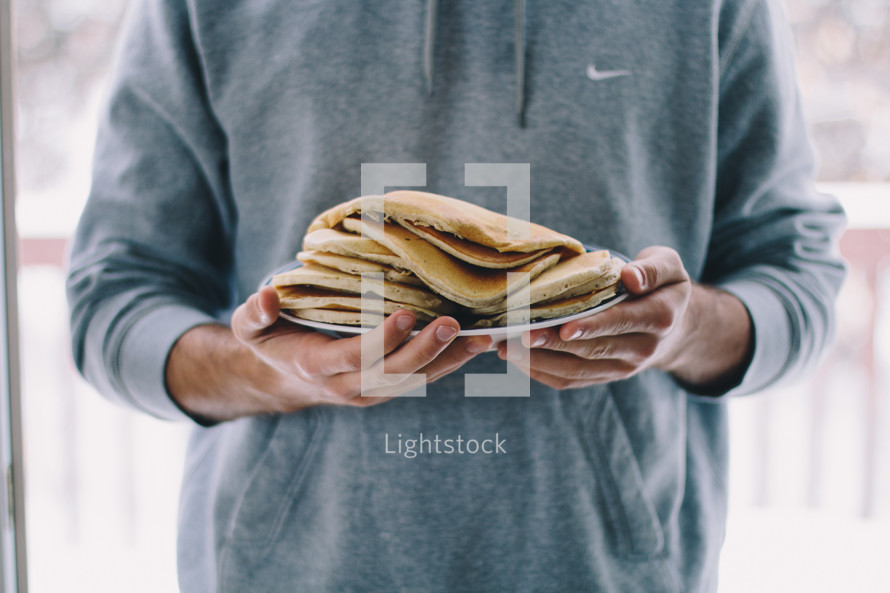 a man holding a plate full of pancakes 