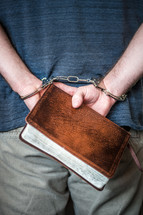 handcuffed man holding a Bible behind his back 