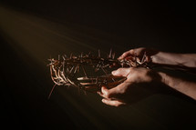 hands holding a crown of thorns in rays of light 