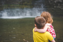brother and sister hugging by a stream 