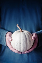 Man holding a white pumpkin in both hands