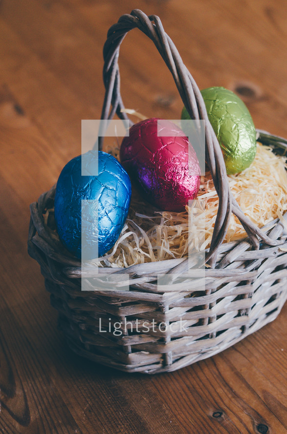 Colored easter eggs in a wicker basket on a wooden table