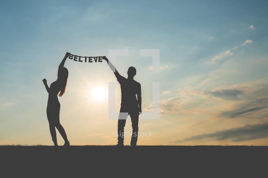 man and woman holding up a silhouette of the word believe 
