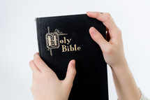 Child's hands holding a closed Bible.