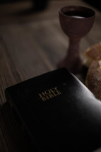 A Bible next to communion bread and wine on a wooden table.