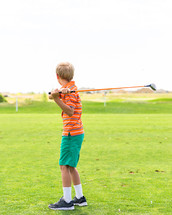 a boy child swinging a golf club 