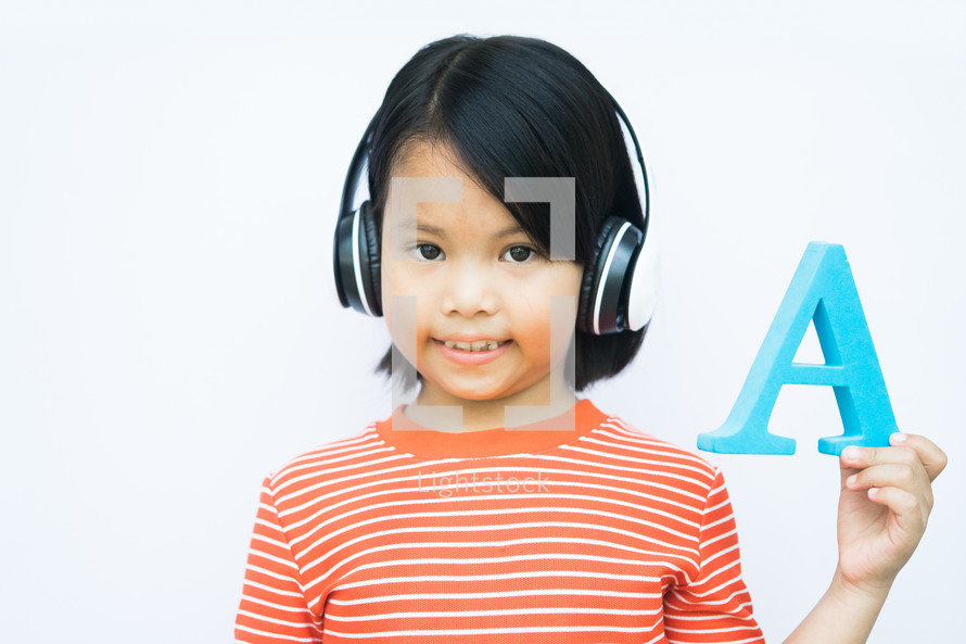 child holding up the letter A with headphones on 