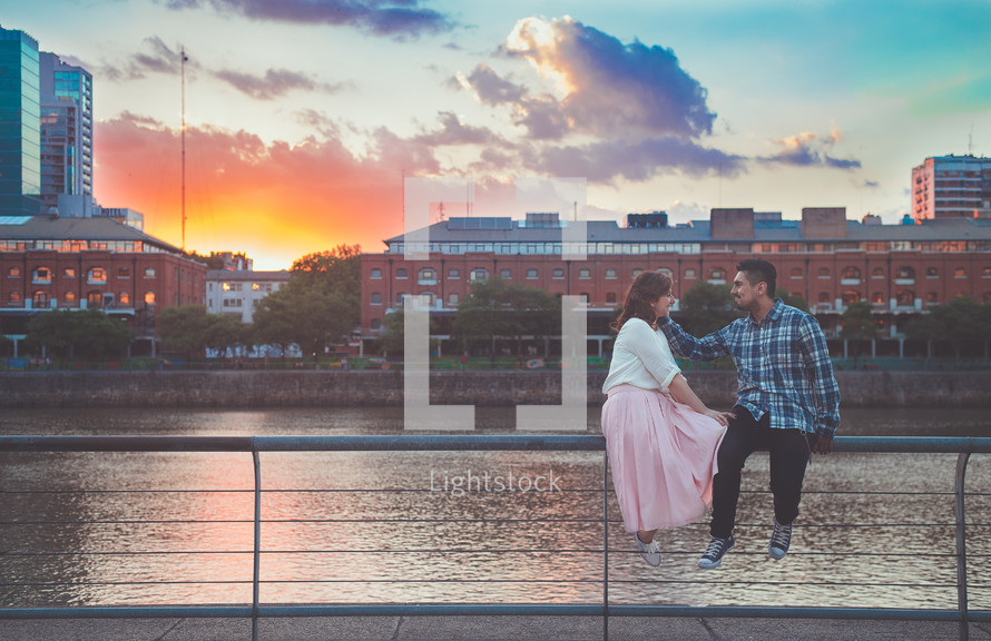 a couple sitting on a railing in front of a river 