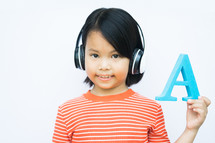 child holding up the letter A with headphones on 