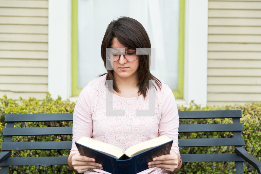 A woman sits on a bench reading a Bible.