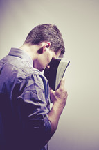 man in prayer to God holding a Bible against his forehead