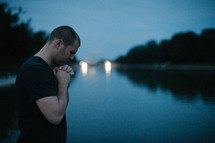 a man in prayer in front of a pond 
