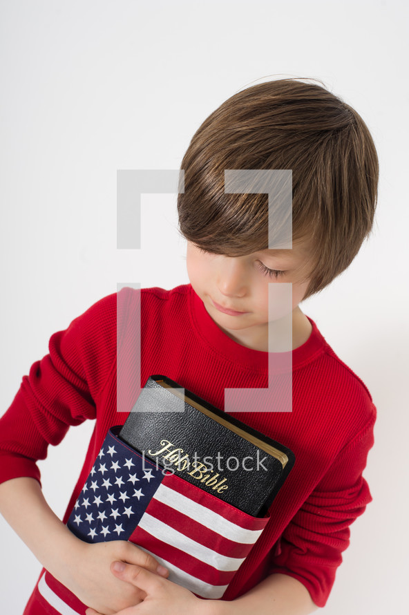 Boy holding a Holy Bible wrapped in an American flag.