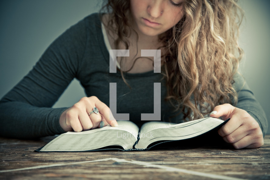 Girl studying Bible open on wooden table.