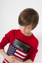 Boy holding a Holy Bible wrapped in an American flag.