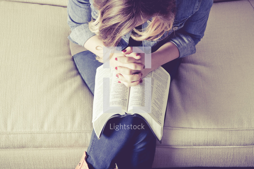 woman with her hands held in prayer over the pages of a Bible