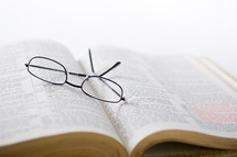 Glasses on the pages of an open Bible.