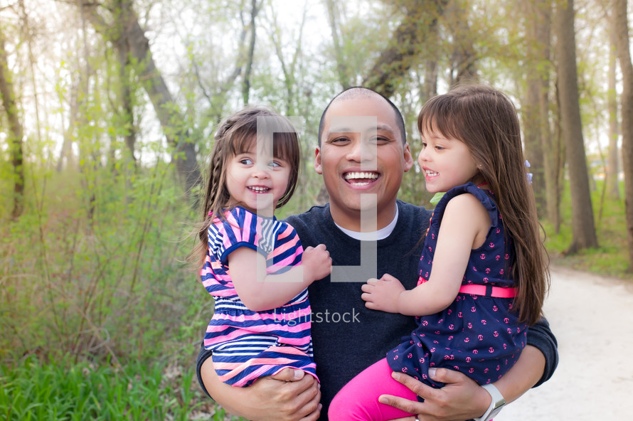 Smiling father standing outside holding his daughters.