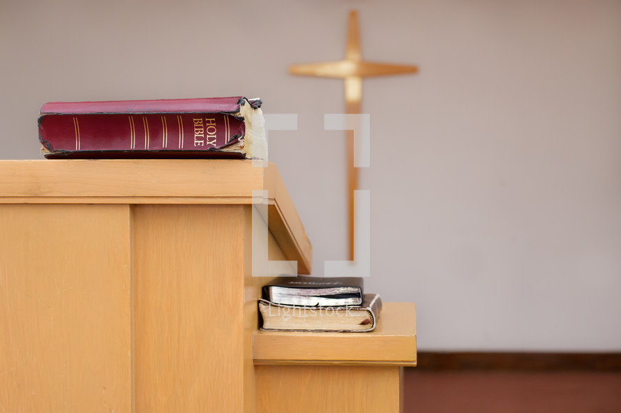 Bibles on the pulpit in front of a cross on the wall.