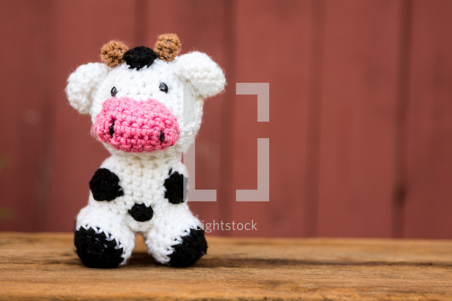 a crocheted cow in front of a red barn