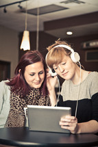 two women listening to music through headphones from an iPad