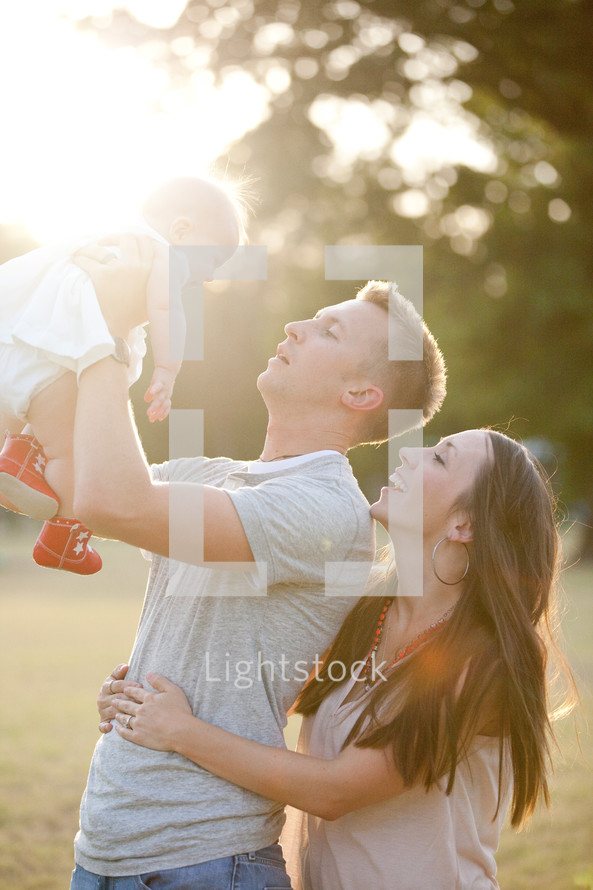 Couple holding infant child up to the sun.