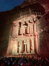 Large group of people sitting on the ground at night, the rock cut architecture of Al Khazneh or The Treasury at Petra, Jordan.