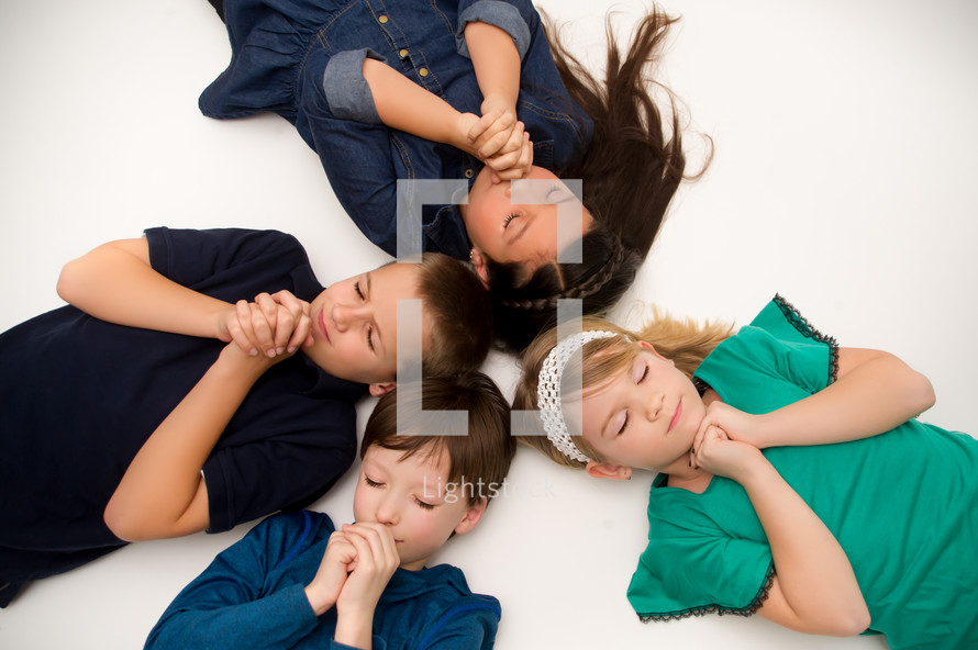 Children praying with their eyes closed while laying on the ground.