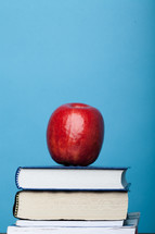 A red apple atop a stack of books with a blue background.