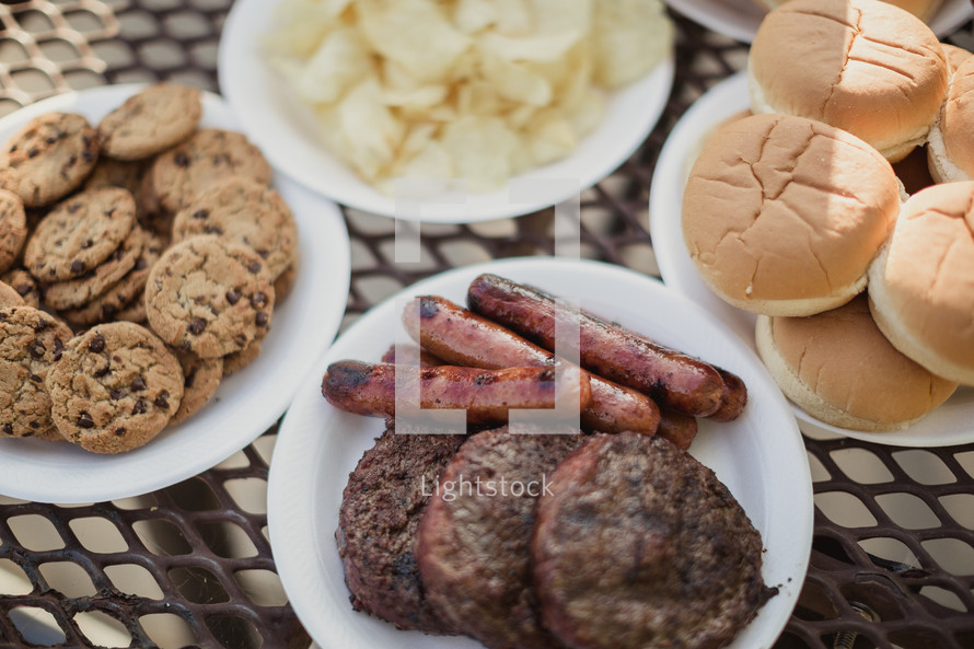 hamburgers and hotdogs on a table outdoors 