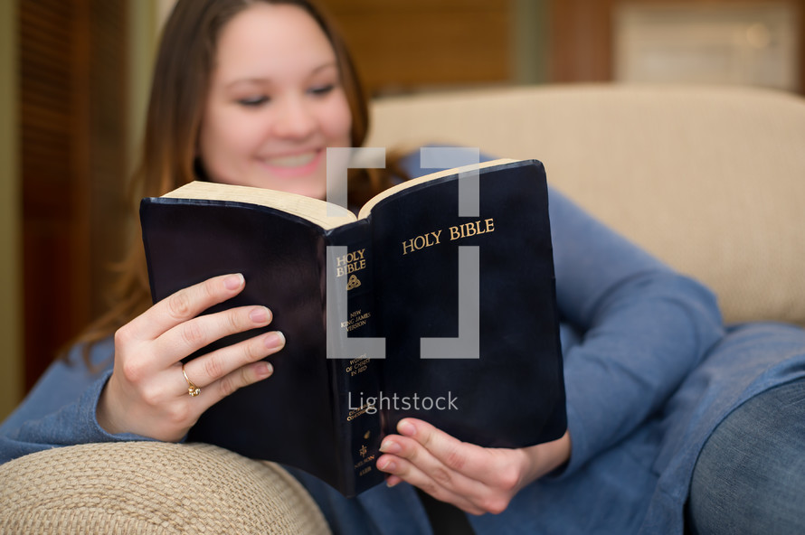 woman lying on a couch reading a Bible