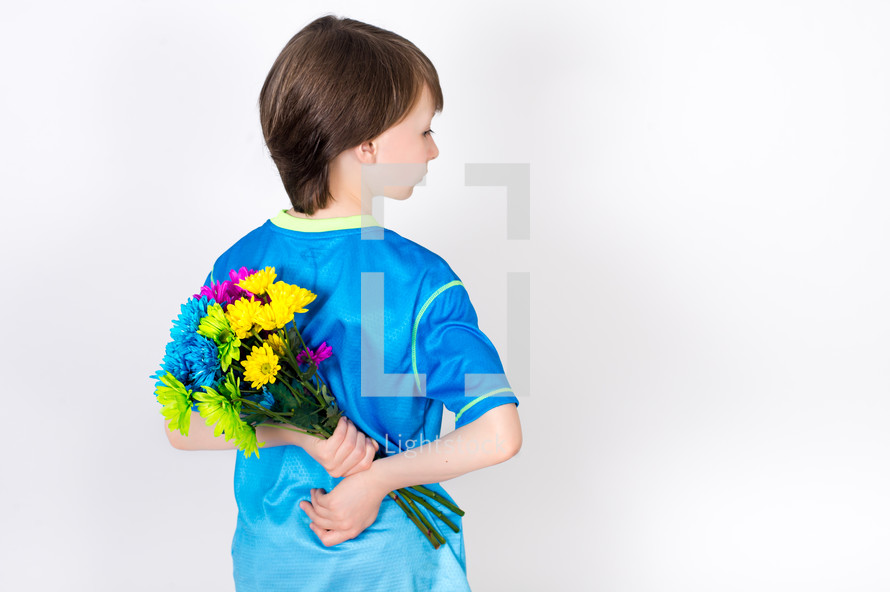 Boy holding a bouquet of flowers behind his back.