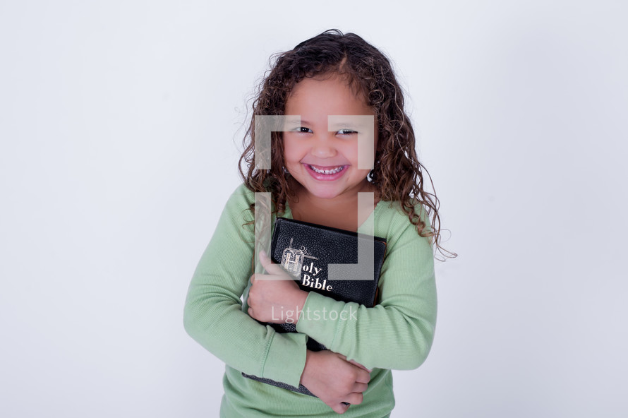 Smiling girl holding a closed Bible.
