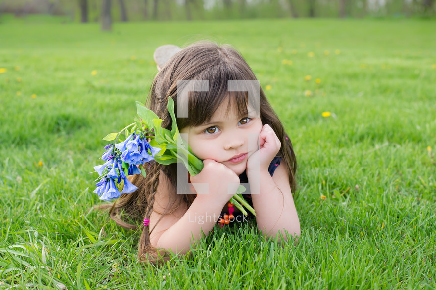 Young girl holding flowers, laying in a field of grass