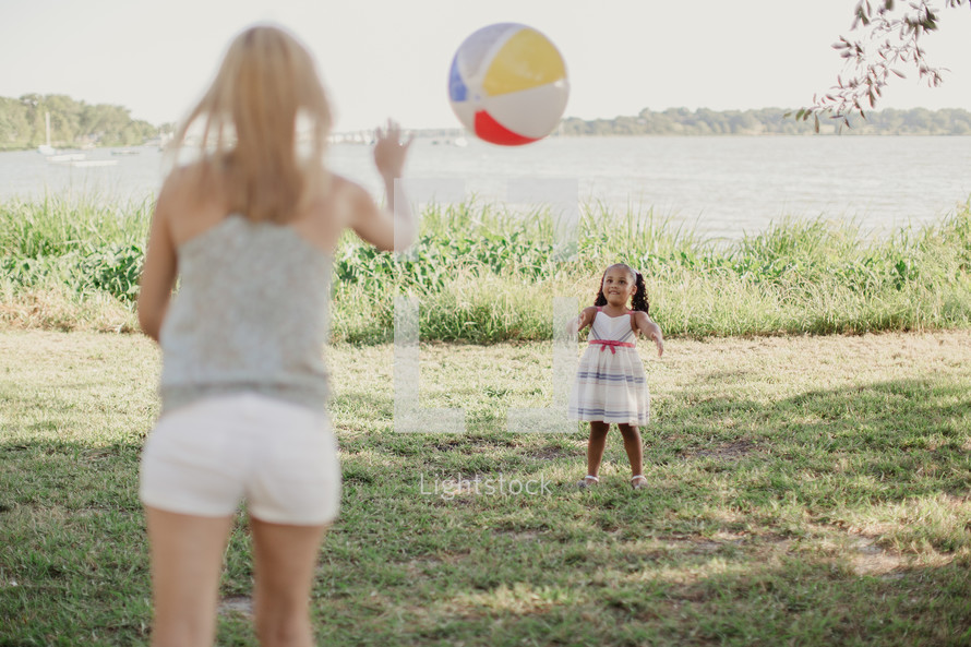 A woman tosses a beach ball to a little girl.