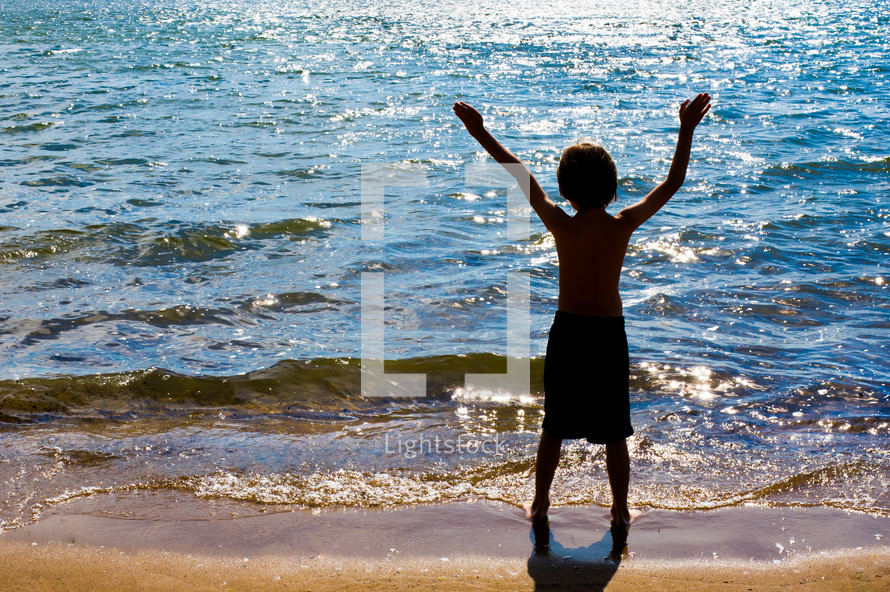 Boy with arms raised while standing at the ocean shore.