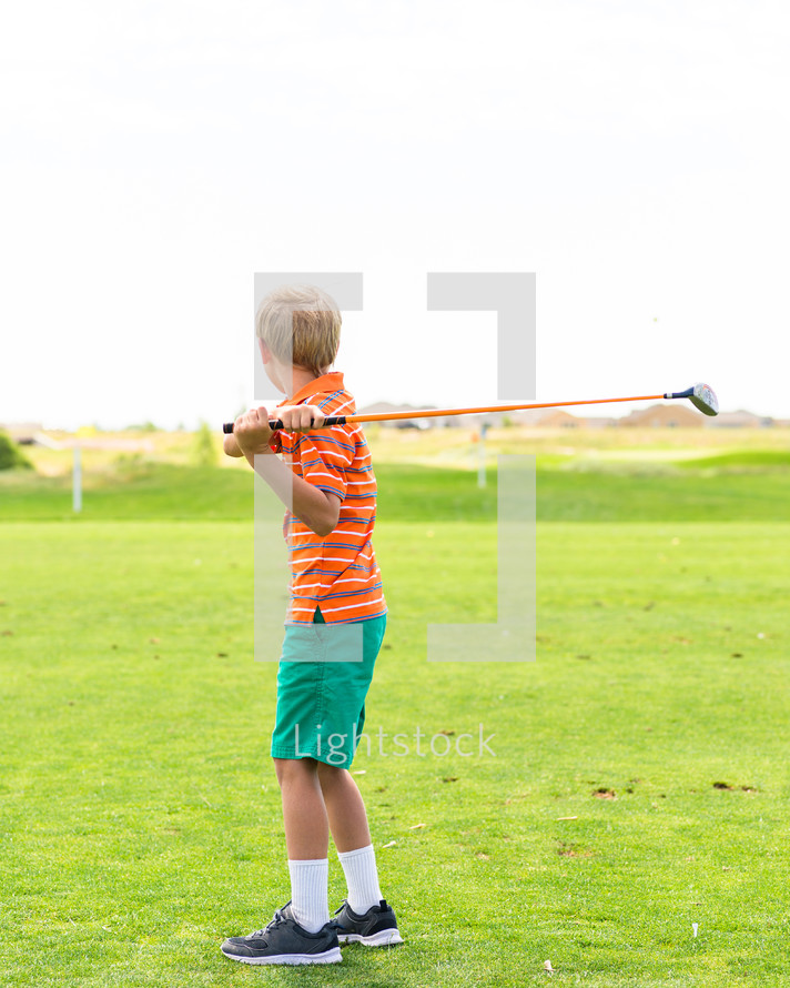 a boy child swinging a golf club 