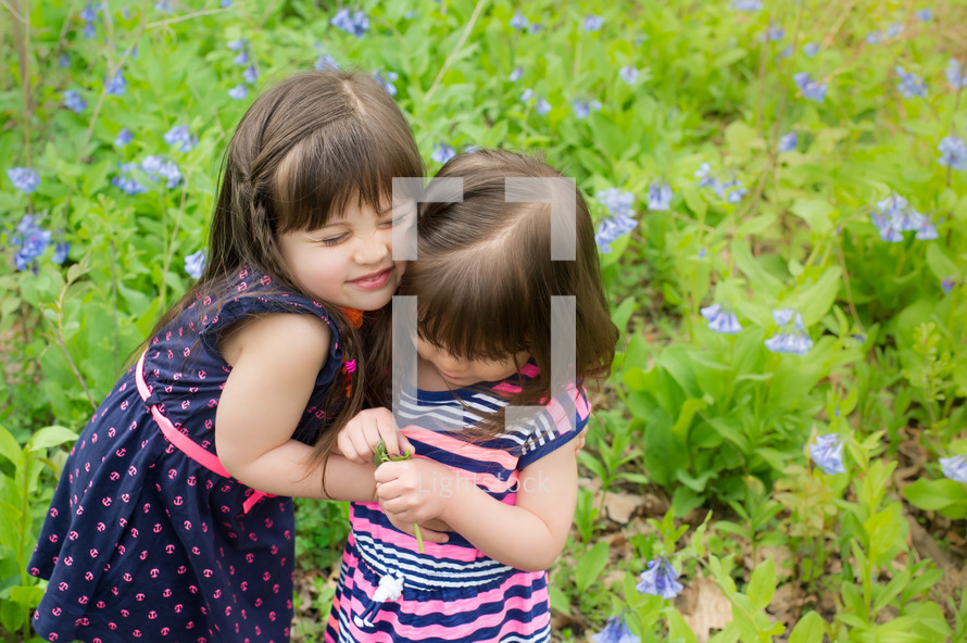 Two young girls standing in a weedy field, hugging