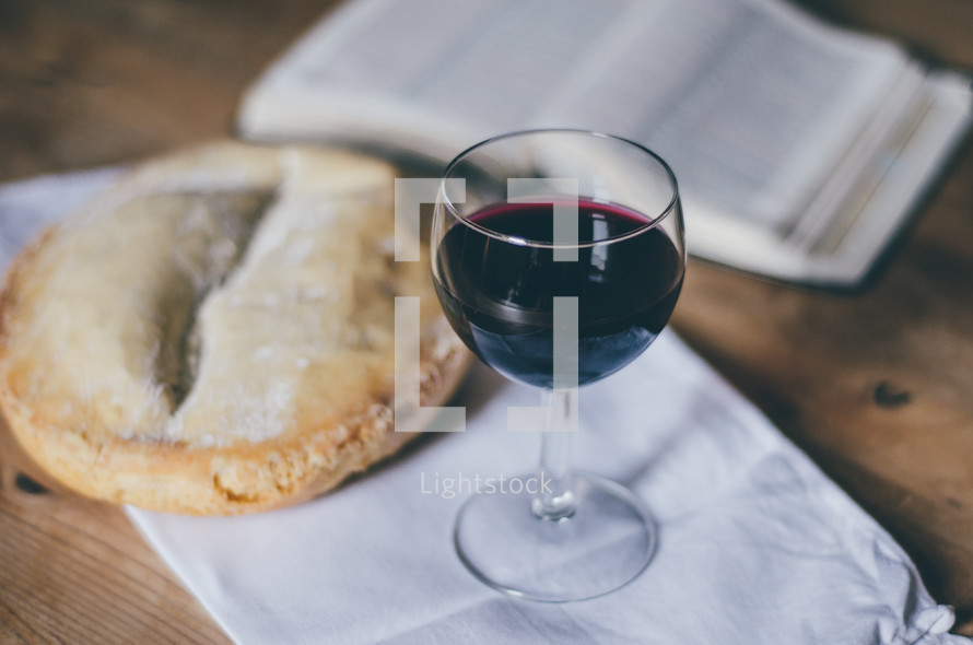 A glass of wine sits on a table next to a loaf of bread and an open bible