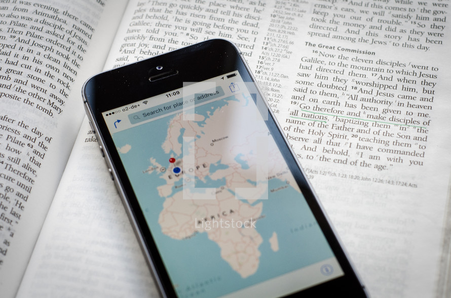A phone with a world map showing Europe & Africa sitting on a bible open to the great commission