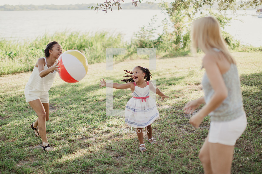 Two women and a little girl playing outdoors with a beach ball.