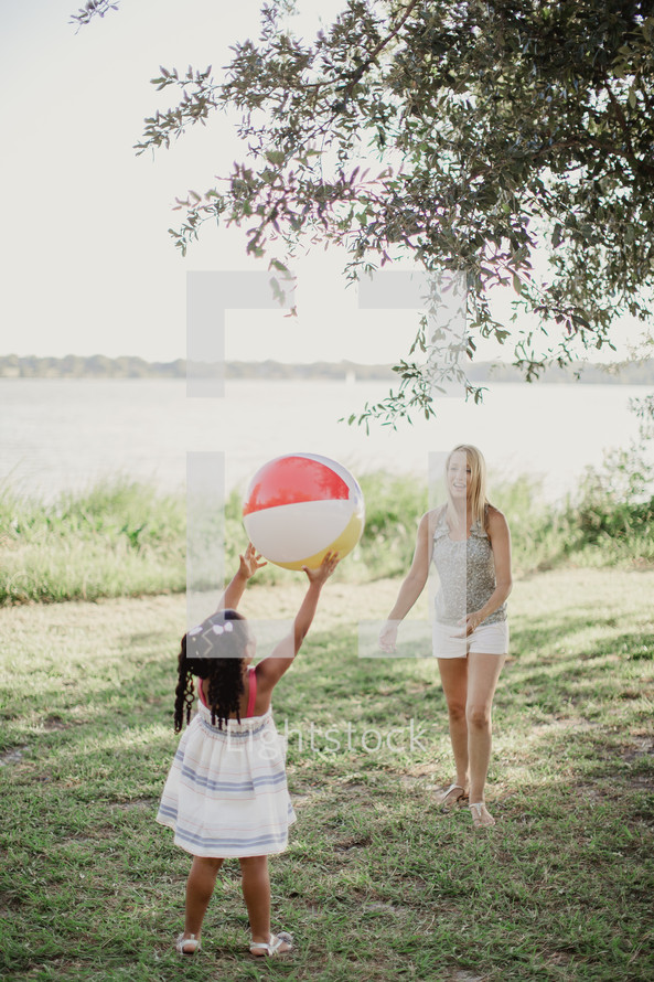 A little girl tosses a beach ball to a young woman.