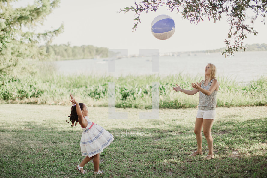 A little girl throwing a beach ball to a young woman.
